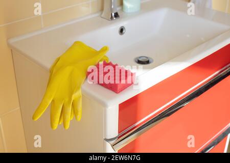 Lavabo e rubinetto per bagno con detergente in guanti di gomma gialla e spugna rosa. Concetto di casalinghi, pulizia, igiene, servizio di pulizia Foto Stock