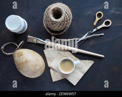 Uovo di Pasqua decorato con tecnica di disaccoppiamento. Strumenti di disaccoppiamento - carta fatta a mano colorata da caffè, pennello, corda, colla e forbici - sul tavolo. Overhead. Foto Stock