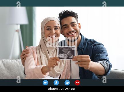 Buone notizie. Allegra coppia musulmana che mostra ultrasuoni bambino durante la videochiamata Foto Stock