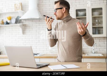 Ritratto del boss di successo che parla sul cellulare durante il lavoro, freelancer in piedi da tavolo, parlando al telefono in cucina leggera, la registrazione di un messaggio vocale, dando compiti ai subordinati, spiega gesturing Foto Stock
