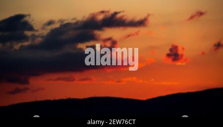 Il tramonto rosso-arancio, dalle nuvole a contrasto, sfocia dietro la silhouette della montagna. Primo piano su un paesaggio estivo luminoso Foto Stock