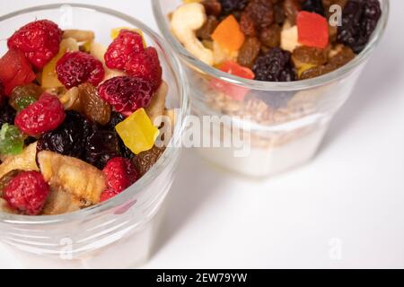 Dessert al muesli con yogurt e frutta candita o secca con lamponi in vetro isolato su sfondo bianco. Prima colazione alla granola Foto Stock