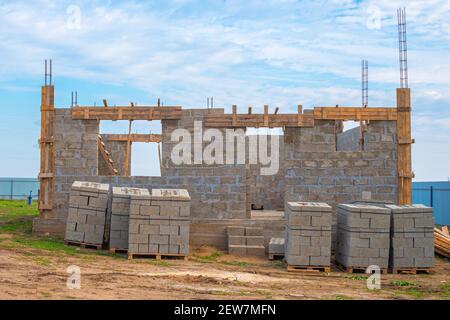 Fasi di costruzione. Casa di campagna in legno di cenere con elementi sporgenti, piano terra. Il materiale da costruzione è impilato su pallet. Foto Stock