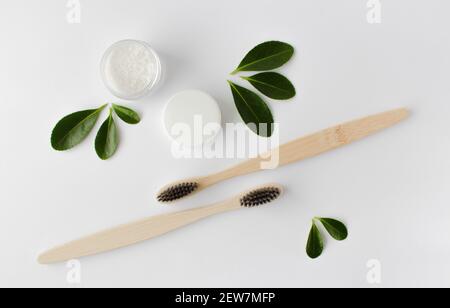 due spazzolini eco-compatibili in bambù di legno, dentifricio e foglie verdi su sfondo bianco. Foto Stock