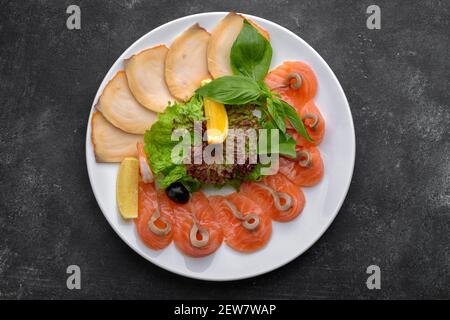 Pesce, a fette sottili, escolar, butteria, salmone, su un piatto bianco con basilico e lattuga, su fondo scuro Foto Stock