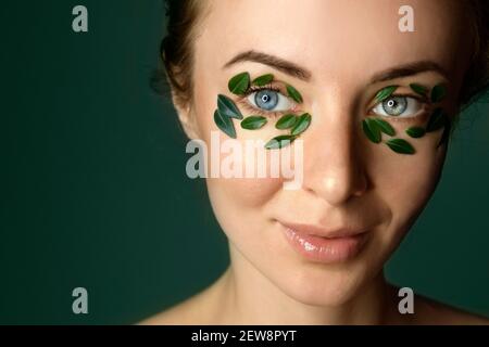 Closeup di giovane donna`s viso con macchie di foglia di bosso. Banner modello spa e benessere per il design. Pubblicità di prodotti cosmetici Foto Stock