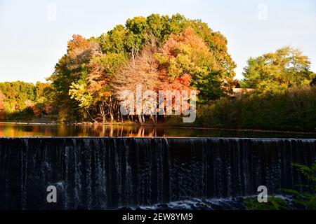 Una brillante esposizione fogliare riflessa in un lago con un cascata durante la luce del tardo pomeriggio Foto Stock