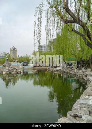 Pechino, Cina - 25 aprile 2010: Quartiere Hujialou Nandi. Laghetto d'acqua verde con piante verdi intorno sotto il cielo d'argento e edificio di appartamenti Foto Stock