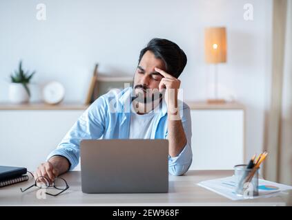 Uomo d'affari arabo overwork che soffre di Emicrania sul lavoro, avendo forte mal di testa Foto Stock