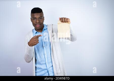 Giovane bell'uomo afroamericano che indossa abiti casual sorridente, sorpreso e puntando borsa di carta Foto Stock