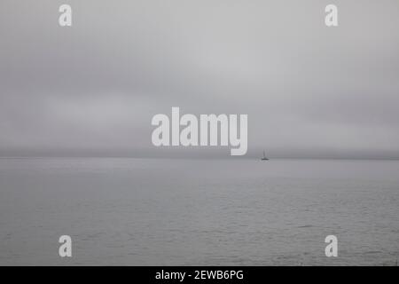 Una singola barca a vela soletta che galleggia all'orizzonte Costa di Long Island New York USA su una nebbia giorno di overcast Foto Stock