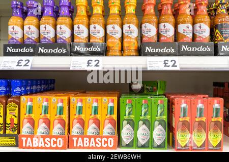Fila di bottiglie di Nando per la sorgente peri peri in esposizione su scaffali insieme a bottiglie di Tabasco sorgente su scaffali per la vendita in supermercato, Regno Unito Foto Stock