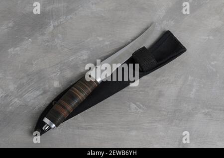 Un elegante coltello da caccia con scabarda e manico in pelle su fondo grigio cemento. Messa a fuoco selettiva. Foto Stock