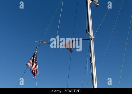 Un rastrello di prato legato tra l'albero di una barca a vela e la running rigging. Una bandiera americana infranta pende in modo impresso dal soggiorno posteriore. Foto Stock