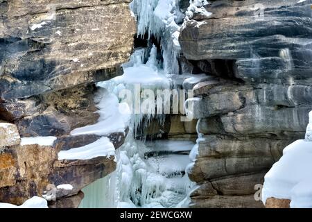Immagine orizzontale di una cascata congelata sull'Athanasca canyon pareti con il ghiaccio e la neve aggrappati a. Rock nella stagione invernale a Jasper National Foto Stock