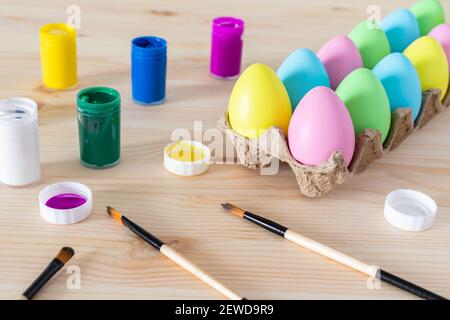 Uova di Pasqua e pitture colorate con pennelli sul tavolo. Concetto di artigianato pasquale. Foto Stock