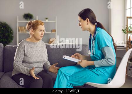 Donna anziana preoccupata seduta sul divano e di cui parla il medico i suoi problemi di salute Foto Stock
