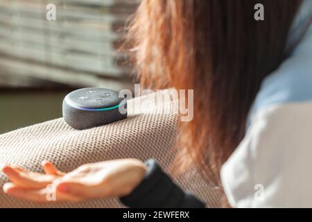 Clarksburg, MD, USA 03-01-2021: Una donna caucasica seduta su una poltrona con vestiti casual a casa sua sta facendo una domanda ad Amazon Echo Dot, voi Foto Stock
