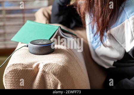 Clarksburg, MD, USA 03-01-2021: Una donna caucasica seduta su una poltrona con vestiti casual a casa sua sta facendo una domanda ad Amazon Echo Dot, voi Foto Stock