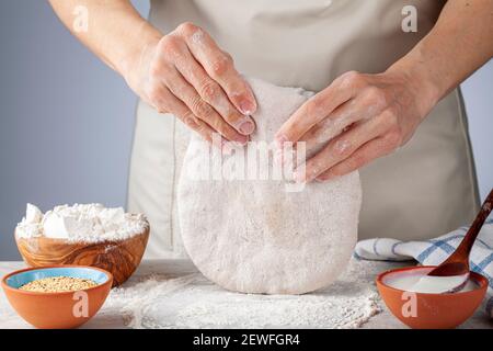 Preparazione di pane piano, pide o pizza basica turche casalingain cucina. Una cuoca donna sta impastando e appiattendo l'intera pasta organica di grano i Foto Stock