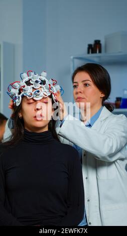 L'assistenza del medico neurologico che mette la cuffia eeg sulle funzioni cerebrali di scaning della testa del paziente, descovering la diagnosi della malattia. Gruppo di ricercatori che lavorano fino a tarda notte in clinica di neurologia Foto Stock