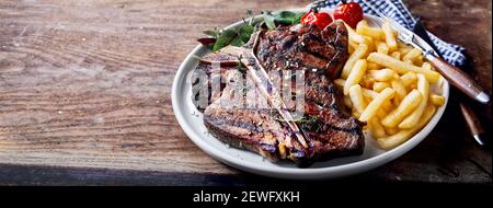 Dall'alto di bistecca di manzo alla griglia con fritto profondo bastoncini di patate e pomodoro con condimenti su tavola di legno Foto Stock