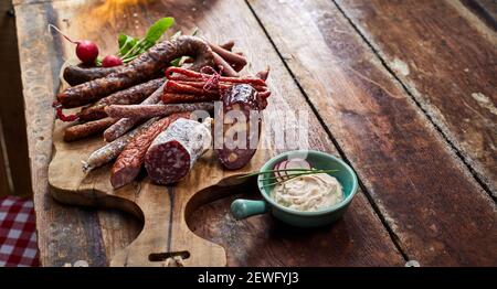 Dall'alto di deliziosi antipasti affumicati e stagionati al taglio sali a bordo vicino al recipiente con formaggio morbido e fette di rafano Foto Stock