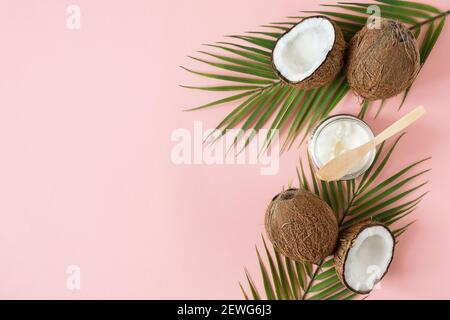 Vasetto di olio di cocco e noci di cocco fresche con foglie di palma su sfondo rosa vista dall'alto con spazio per la copia. Foto Stock