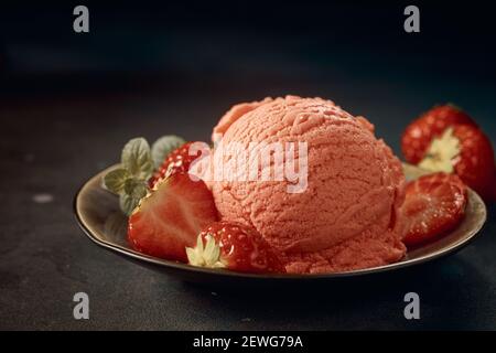 Dall'alto di appetitoso cucchiaio di gelato rosa servito sopra piatto e decorato con fragole fresche Foto Stock