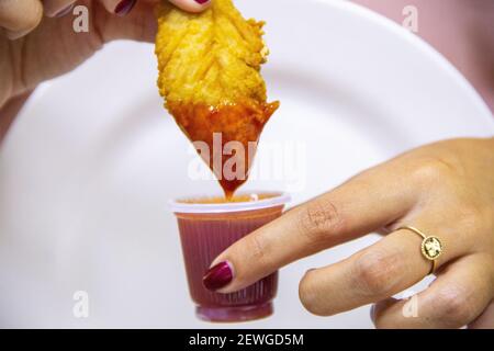 Un closeup colpo di mani di una donna che tuffano croccante fritto pepite di pollo in salsa al barbecue Foto Stock