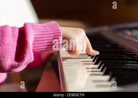 Primo piano della mano del bambino sui tasti del pianoforte o del sintetizzatore, vista laterale. Foto Stock