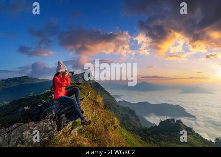 Viaggiatore seduto sulla roccia e tenendo la macchina fotografica scattare foto alle montagne di Doi pha mon a Chiang rai, Thailandia. Foto Stock