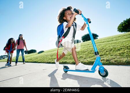 Ragazzo di sei anni su uno scooter, seguito da sua sorella Foto Stock