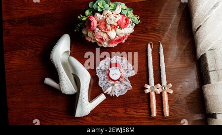 Mattina della sposa. Bouquet nuziale. Candele di nozze nella chiesa. Anelli di nozze in una scatola rossa. Scarpe bianche della sposa. Garter sulla gamba del br Foto Stock