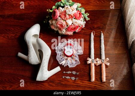 Mattina della sposa. Bouquet nuziale. Candele di nozze nella chiesa. Anelli di nozze in una scatola rossa. Scarpe bianche della sposa. Garter sulla gamba del br Foto Stock