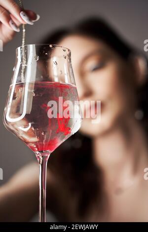 Gocce di vernice rossa del sangue in un bicchiere d'acqua, una donna guarda il bicchiere. Foto Stock