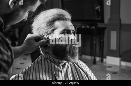 Uomo al barbiere. Parrucchiere. Barbiere e cliente professionale. Rifinitura della barba da vicino. Mantenimento della forma della barba. Migliora la tua esperienza di taglio dei capelli. Capelli facciali. Crescere barba e baffi. Foto Stock