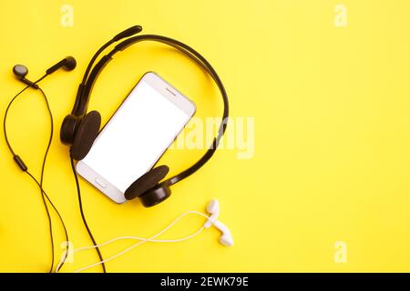 Cuffie e smartphone su sfondo giallo. Concetto di social media clubhouse. Simulazione, spazio per la copia, disposizione piatta, vista dall'alto Foto Stock