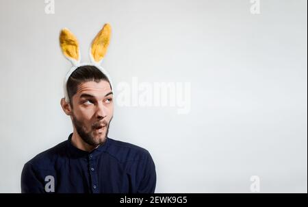 L'uomo caucasico con le orecchie di coniglio peluche gialle si siede e guarda via a sorpresa. Un banner creativo a colori per Pasqua e luogo per il tuo testo e pubblicità Foto Stock