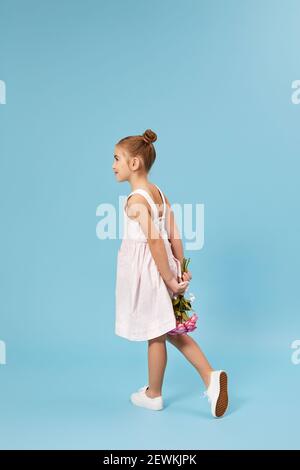 bambina con bouquet di rose dietro la schiena su sfondo blu studio. vista posteriore Foto Stock