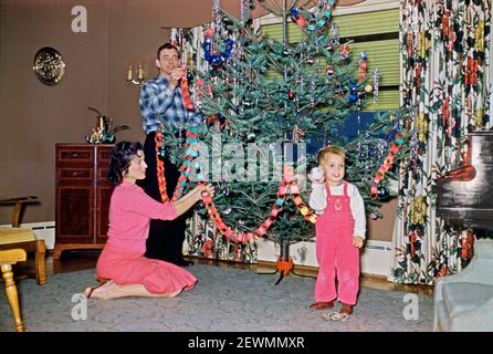 Mettere le decorazioni di Natale sull'albero, in un soggiorno negli Stati Uniti nel 1958. Le decorazioni tradizionali per il grande albero includono la ginspilla, i garlands di carta collegati e i baubles, uno dei quali il ragazzo sta tenendo. Questa immagine è tratta da un vecchio lucido a colori americano dilettante Kodak – una fotografia degli anni '50. Foto Stock