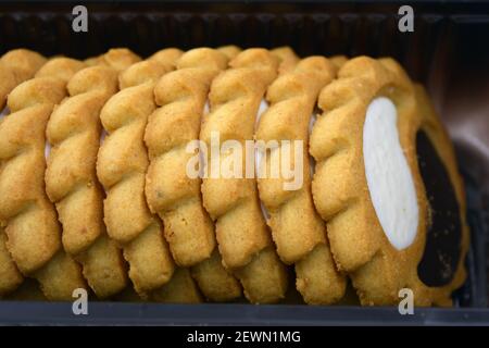 Deliziosi biscotti sabbiosi con bordi taglienti e cioccolato e riempitivo bianco investiti in confezioni marrone. Foto Stock