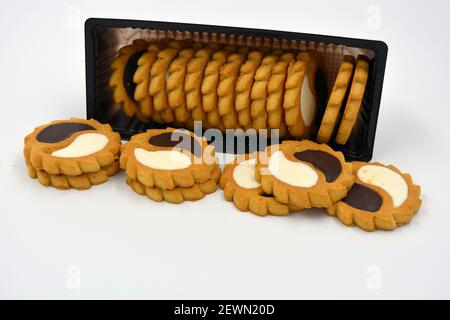 Deliziosi biscotti sabbiosi con bordi taglienti e cioccolato e riempitivo bianco investiti in confezioni marrone. Foto Stock