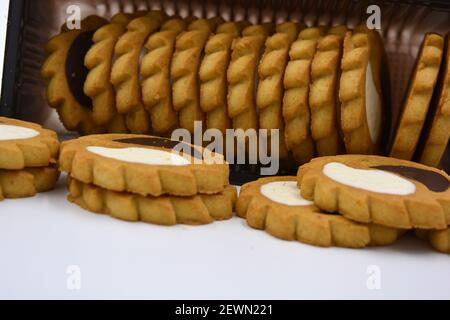 Deliziosi biscotti sabbiosi con bordi taglienti e cioccolato e riempitivo bianco investiti in confezioni marrone. Foto Stock