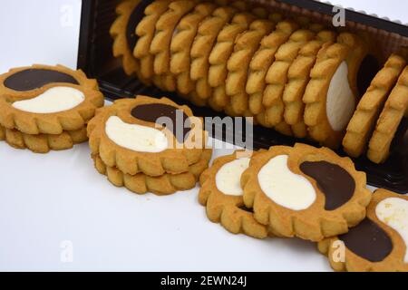 Deliziosi biscotti sabbiosi con bordi taglienti e cioccolato e riempitivo bianco investiti in confezioni marrone. Foto Stock