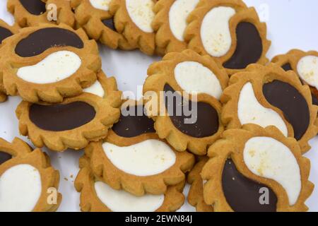 Biscotto di sicurezza sotto forma di sole con stucco bianco e cioccolato, dolce sotto forma di due gocce poste su fondo bianco. Foto Stock