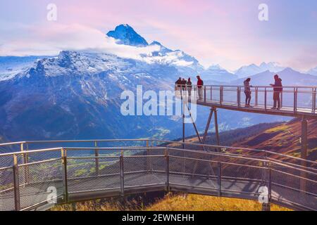 Grindelwald, Svizzera - 10 ottobre 2019: Persone sulla scogliera cielo passeggiata ponte di metallo al primo picco delle Alpi svizzere montagna, cime di neve rosa tramonto panorama Foto Stock