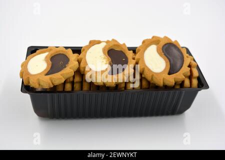 Deliziosi biscotti sabbiosi con bordi taglienti e cioccolato e riempitivo bianco investiti in confezioni marrone. Foto Stock