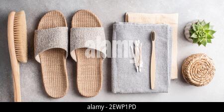 Eco spa e accessori per il bagno di bellezza su sfondo grigio in pietra. Pantofole di bambù, spazzola anticellulite, asciugamani, spazzolino da carbone, bambù ea Foto Stock