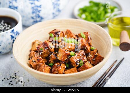 Tofu di teriyaki fritto vegano con scalioni e semi di sesamo in ciotola di bambù. Cucina asiatica Foto Stock